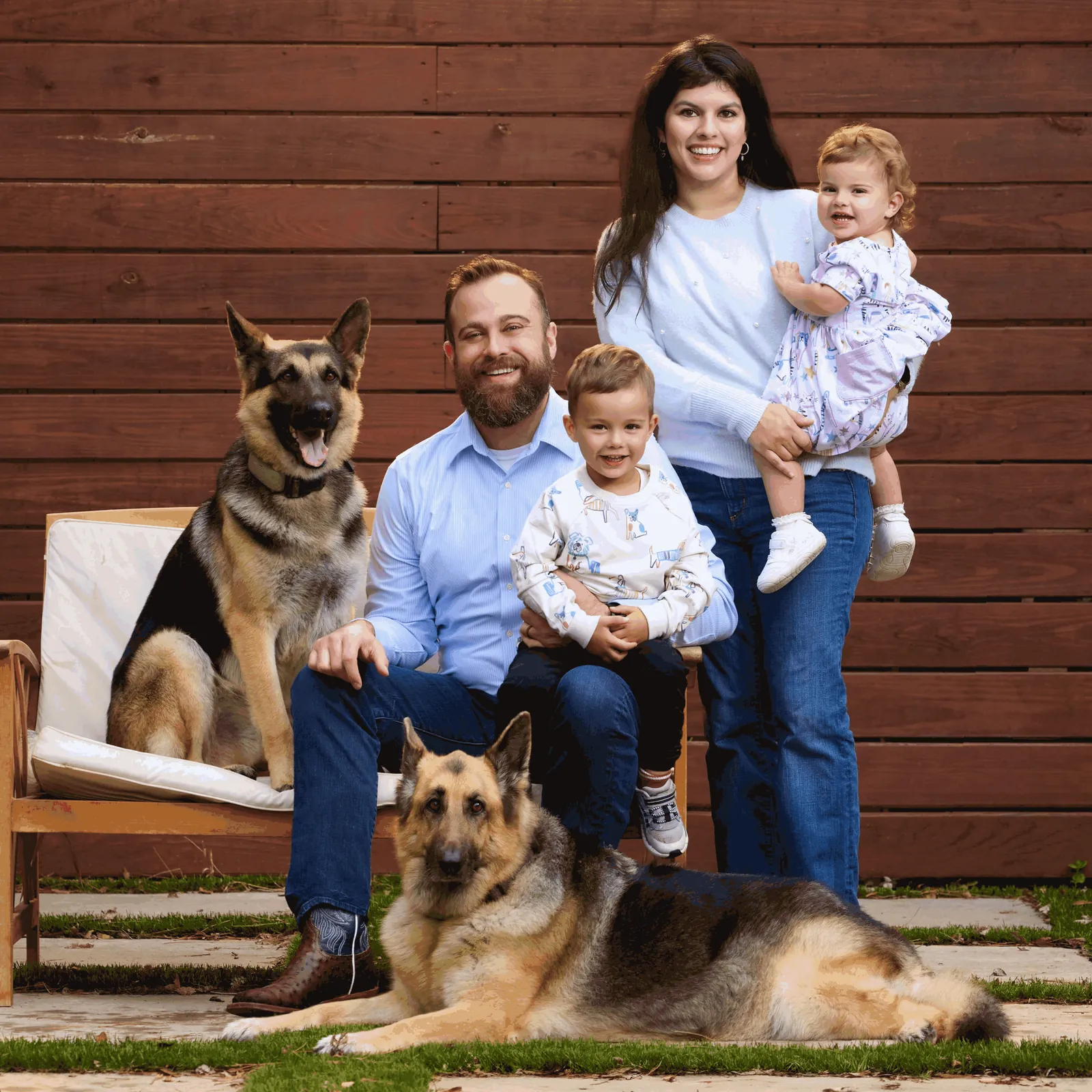 Philip, his wife, their two young children, and two German Shepherds in front of a wooden fence. Shelby lies in front.